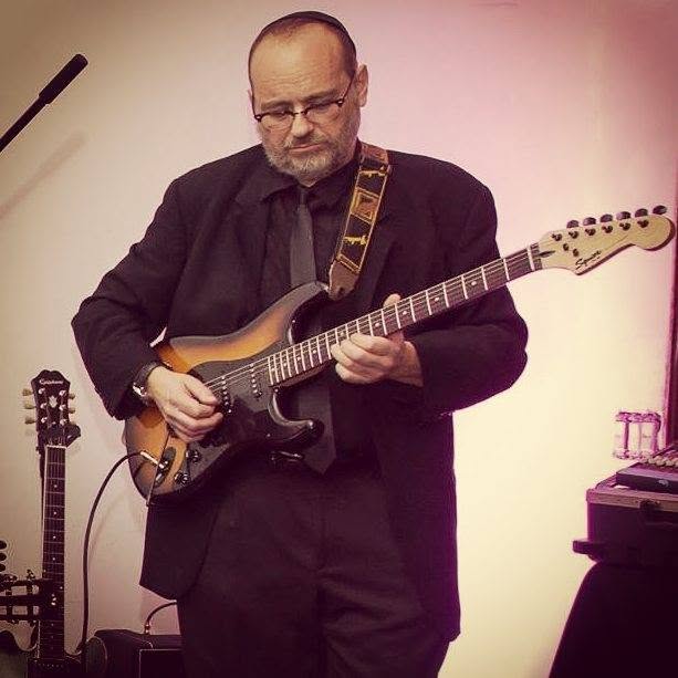 Moshe Antelis playing electric guitar in a suit